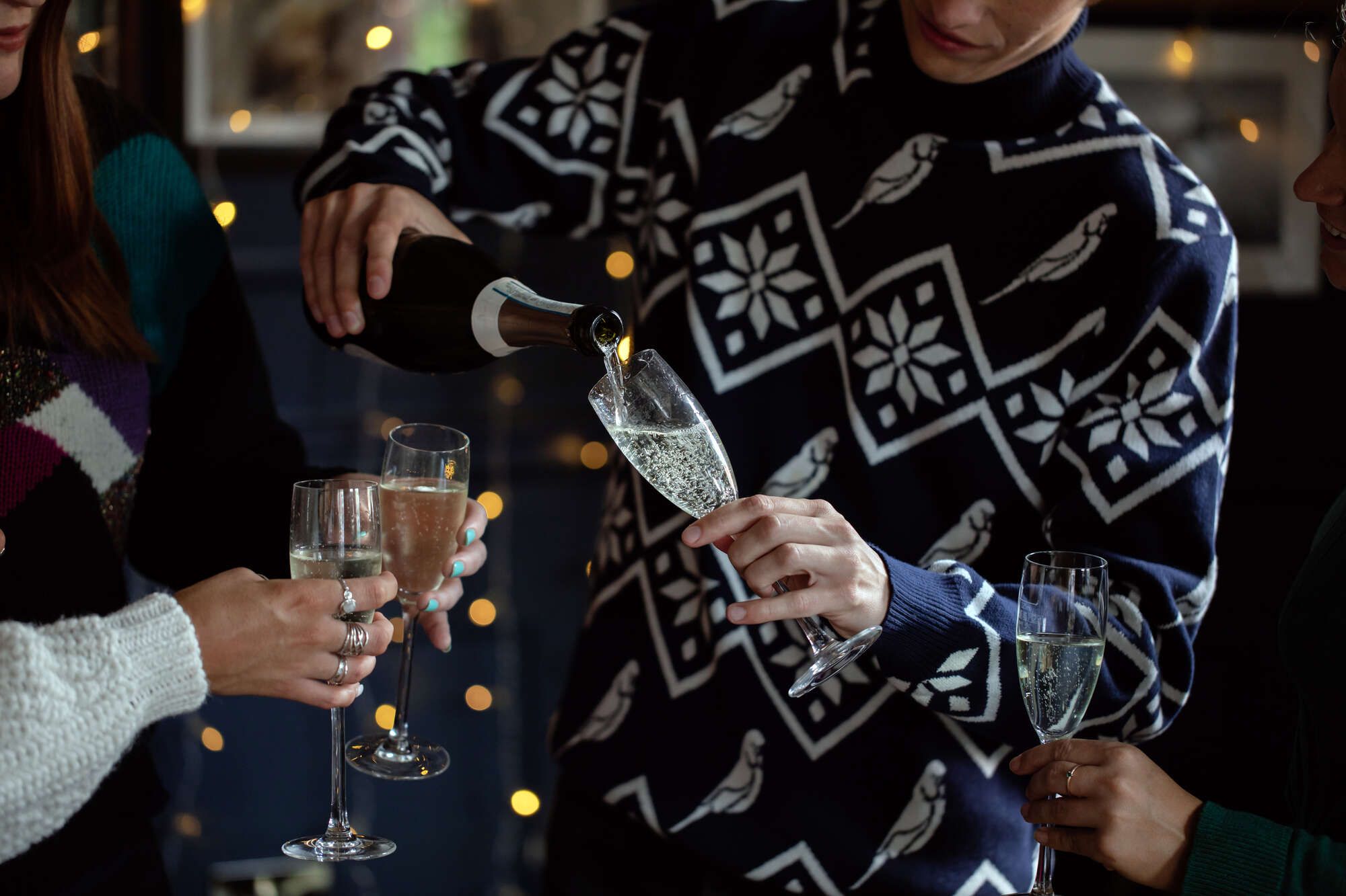 Man pouring Champagne and topping up friends glasses in a Christmas jumper, Bristol