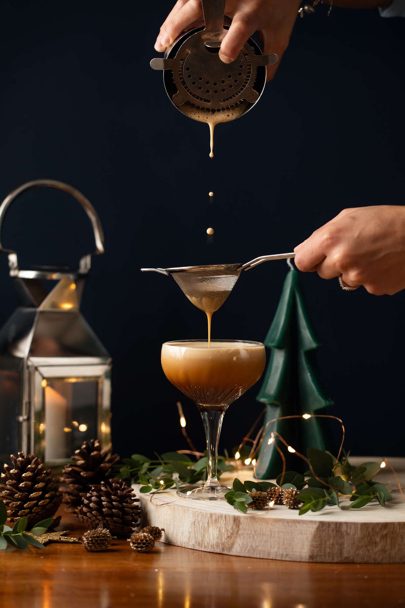 Espresso Martini being poured in an elaborate fashion. With a candle lantern & Christmas tree