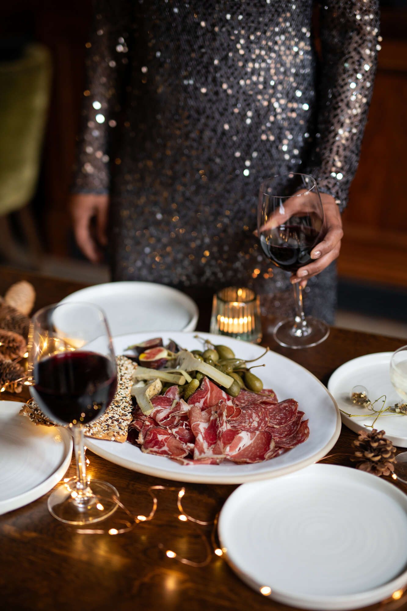 Lady in sparkling NYE dress with a charcuterie board and red wine and festive lights in Bristol